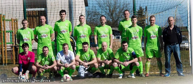 Eine Gruppe von Männern in grünen T-Shirts steht auf einem Fußballfeld, einige sind in der Hocke, mit einem Ball vor ihnen und einem Torpfosten rechts daneben.
