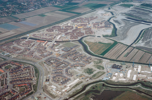 Luftaufnahme einer Stadt mit dichtem Baumbestand, Straßen, Feldern, Bäumen und einem zentralen Reservoir, umgeben von urbanen Gebieten.