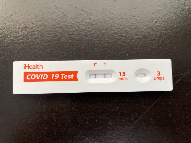 Schwarze Oberfläche mit einem weißen und roten Covid-19-Testthermometer, das Text und Zahlen anzeigt.
