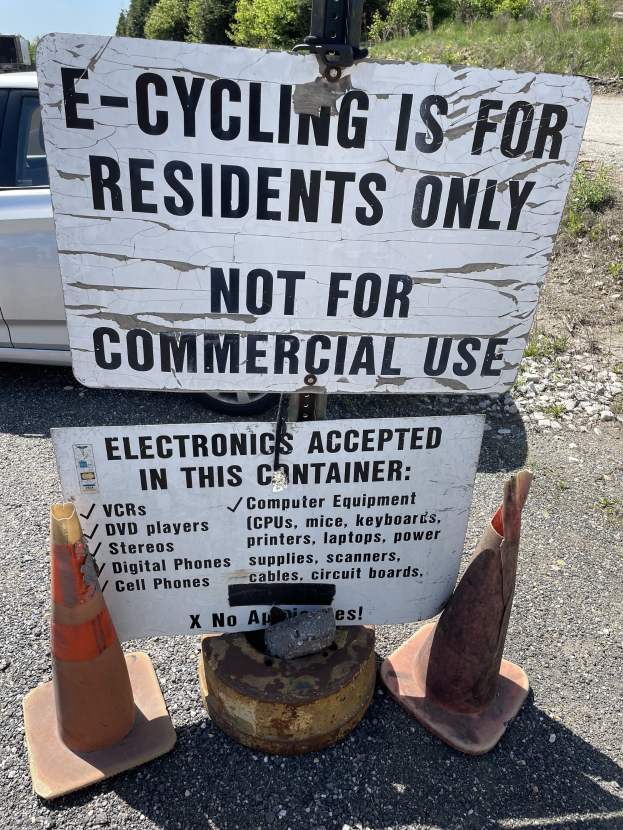 Schild mit Aufschrift 'e-Bike nur für Anwohner' neben einer Straße mit Verkehrskegeln, einem Fahrzeug, Bäumen und einem klaren blauen Himmel im Hintergrund.