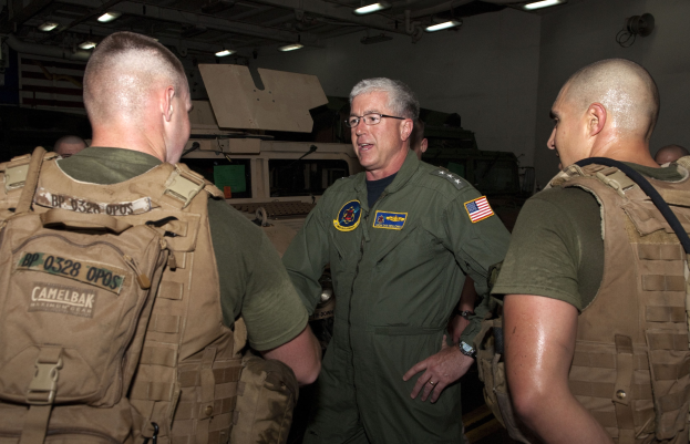 Eine Gruppe von Männern in militärischen Uniformen, die vor einer beleuchteten Wand sprechen, mit einem Kommandeur in der Mitte.