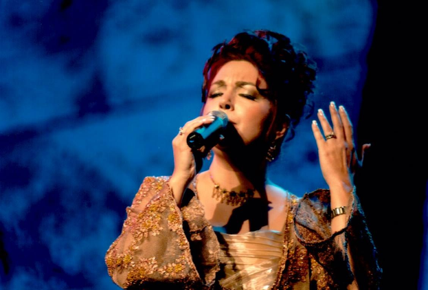 Frau in goldenem Kleid singend ins Mikrofon auf einer Bühne mit blau-schwarzem Hintergrund, die bei der Eurovision singt.