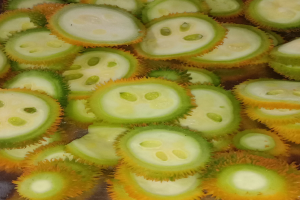 Nahaufnahme einer runden, stacheligen Durian-Frucht mit gelbgrüner Außenseite und weißem Inneren, die auf einem Tisch liegt.