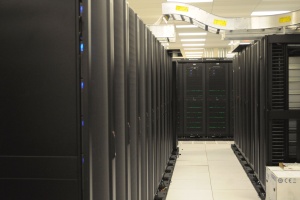 Ein Rechenzentrum mit einer Reihe von Servern, beleuchtet von Deckenlampen, ordentlich und gut beleuchtet.