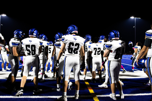 Eine Gruppe von Fussballspielern in Helmen und Stiefeln steht auf einem Feld unter Flutlichtmasten, bereit für ein Spiel.