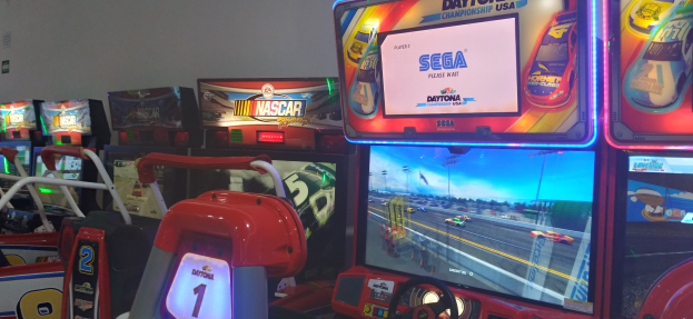 Eine Reihe von buntfarbenen Arcade-Rennwagen-Maschinen in einem Raum mit einer Wand im Hintergrund.