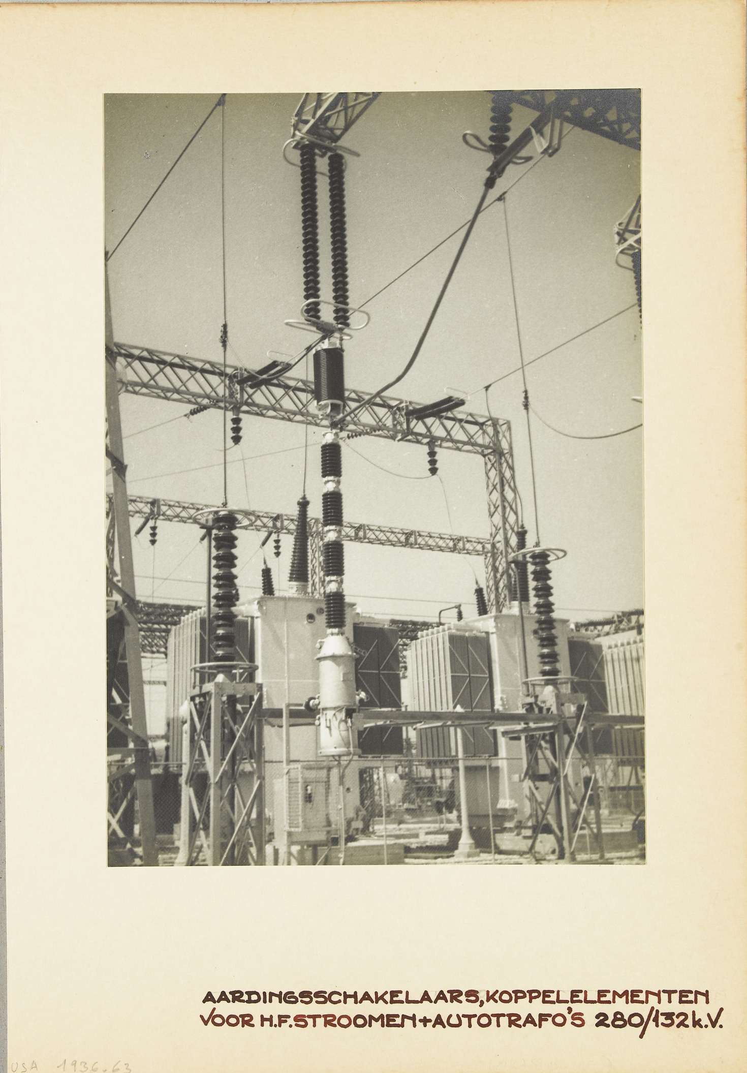 Ein altes Schwarz-Weiß-Foto einer elektrischen Umspannstation mit sichtbaren Transformatoren, Drähten und Text am unteren Rand.