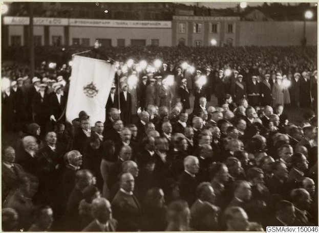 Schwarzes und weißes Bild einer großen Menge vor einem Gebäude, mit einer Person, die eine Fahne hält, in der Mitte, Polen und Lichter im Hintergrund und Text unten, der "Gustav Klimts Rede an der Berliner Mauer" lautet.
