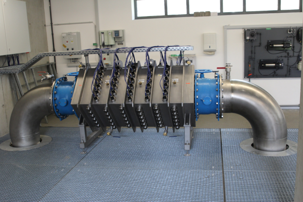 Großer Industrie-Wärmetauscher in einem Gebäude mit Fenstern oben, verbunden mit verschiedenen Komponenten und Kabeln.