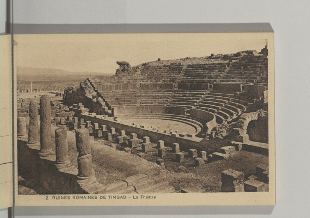 Schwarzes und weißes Foto der Ruinen eines römischen Amphitheaters in Timbuktu, Türkei, das Säulen, Treppen und Text am Boden zeigt.
