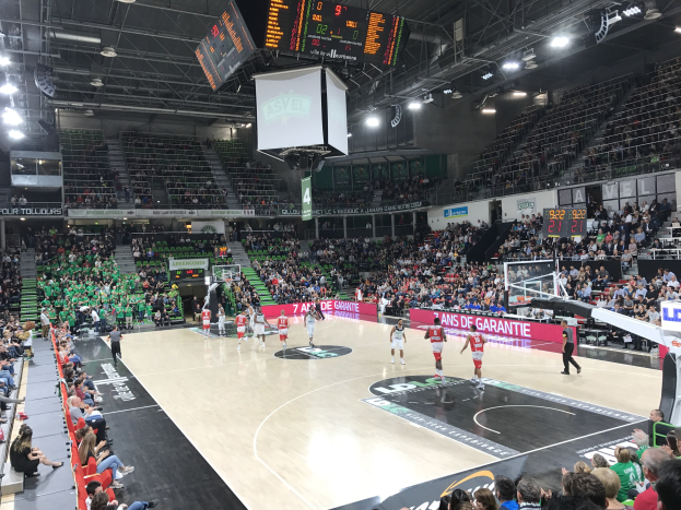 Basketballspiel in einer großen Arena mit Zuschauern, mit einem Scoreboard, das "Asvel vs Galatasaray" anzeigt