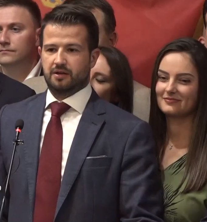 Ein Mann im Anzug spricht an einem Rednerpult mit einem Mikrofon zu einer Menge hinter einem Banner, wahrscheinlich in Reaktion auf ein Regierungssozialmedienverbot.