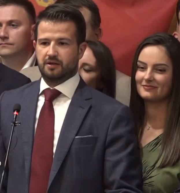 Ein Mann im Anzug spricht an einem Rednerpult mit einem Mikrofon zu einer Menge hinter einem Banner, wahrscheinlich in Reaktion auf ein Regierungssozialmedienverbot.