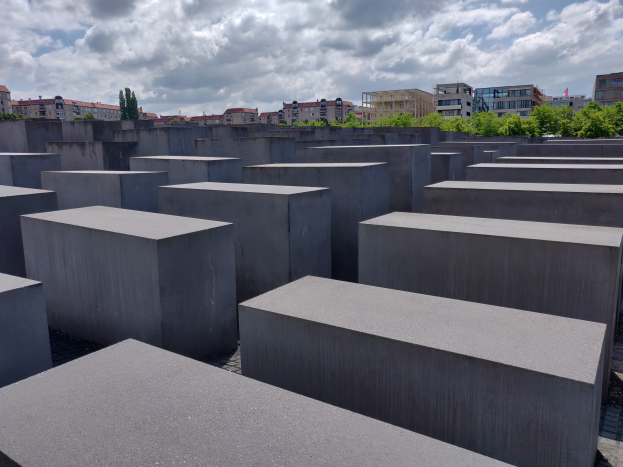 Luftaufnahme des Holocaust-Mahnmals für die ermordeten Juden Europas, mit einem Gittermuster aus Betonsteinen, Bäumen, Gebäuden und Wolken im Hintergrund.