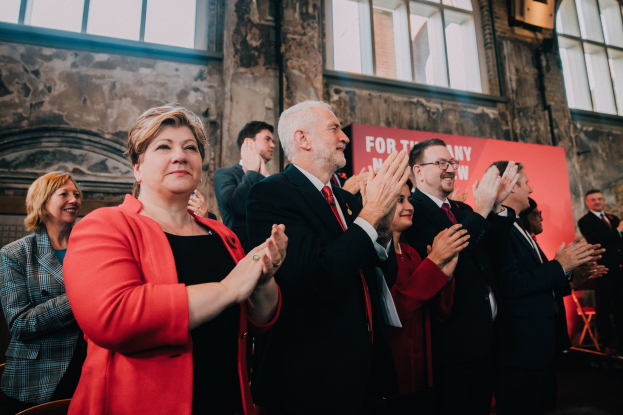 Gruppe von Menschen, die vor einer Menge jubeln, mit einem Banner im Hintergrund, das einen Wahlsieg anzeigt.