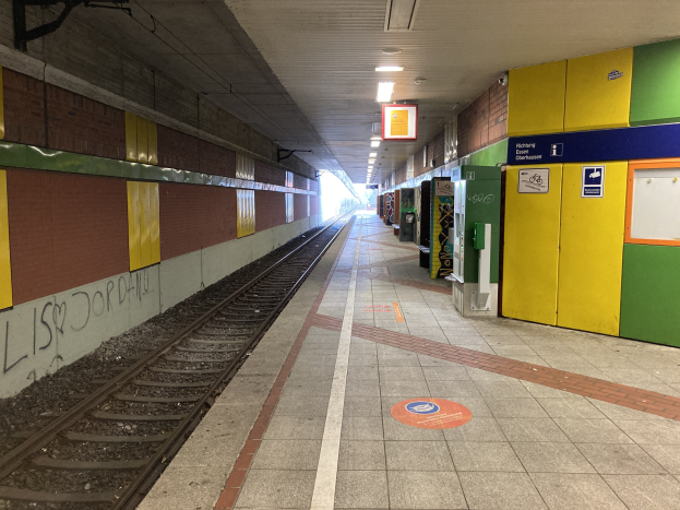 Ein Bahnsteig in Berlin Hauptbahnhof, Deutschland, mit einem Zug auf den Schienen, beleuchtet von Deckenlampen, einer Graffiti-beschmierten Wand auf der linken Seite und ein paar Gegenständen auf der rechten Seite.