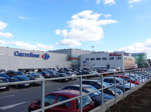 Großes Autohaus mit zahlreichen Fahrzeugen vor der Tür, umgeben von städtischen Gebäuden, Straßeninfrastruktur und einem bewölkten Himmel.