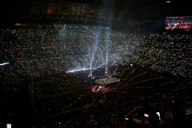 Große Menschenmenge in einem hell erleuchteten Stadion bei Nacht, mit einem Bildschirm rechts, der die Ergebnisse der Super Bowl XLVII-Halbzeitshow anzeigt.