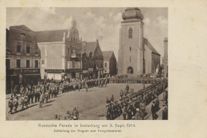 Ein Schwarz-Weiß-Foto eines Umzugs in Insterburg am 5. September 1914, das viele Menschen, Gebäude mit Fenstern im Hintergrund und bewölkten Himmel zeigt, mit Text am unteren Bildrand.