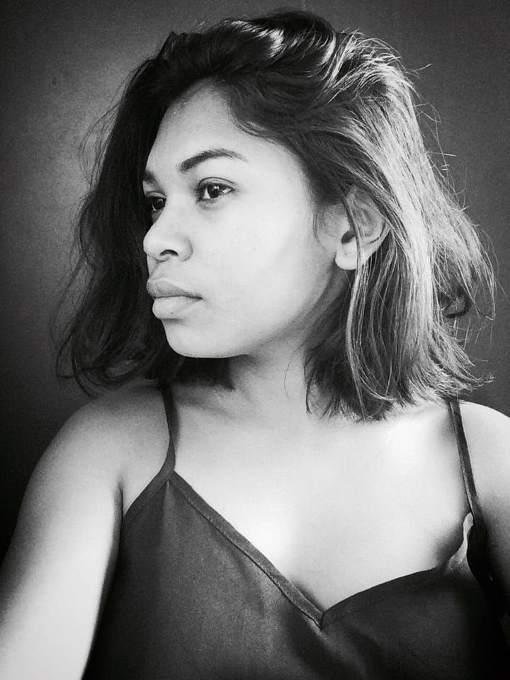 Eine selbstbewusste Frau in einem schwarzen Kleid posiert in einem Schwarz-Weiß-Foto, steht mit einer eleganten Haltung vor einer Wand und trägt einen sleek Bob und dezenten Make-up.