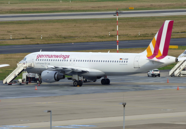 Germanwings Airbus A320-200 am Frankfurter Flughafen geparkt mit Bodenfahrzeugen, Verkehrskegeln, Versorgungsmasten und Gras im Hintergrund.