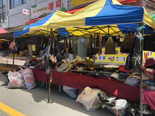 Ein Markt mit Zelten, die Taschen, Hüte und andere Artikel präsentieren, vor Häusern mit Fenstern und Texttafeln.