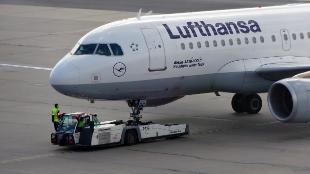 Ein Lufthansa Airbus A319-100 auf der Rollbahn am Frankfurter Flughafen, mit einem Bodenfahrzeug und einer Person in der Nähe, bereit zum Start.