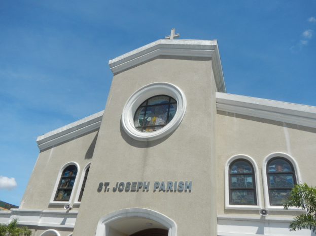 St. Joseph Parish Church in Key West, Florida, a building with windows and a cross on top, surrounded by trees with a sky filled with white, fluffy clouds in the background.