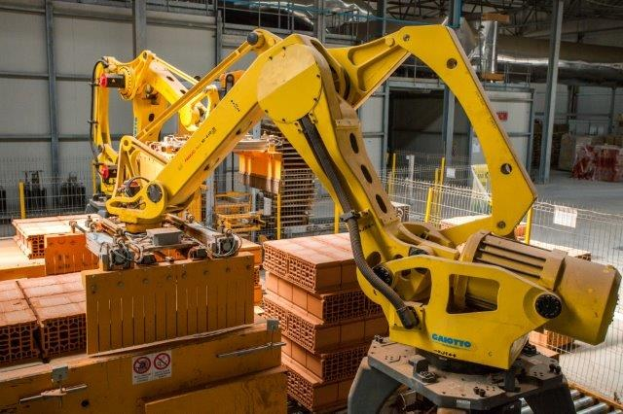 Großes Industrie-Lager mit gestapelten Kisten, Kränen an der Decke, Zaun, Strommasten und einer fernen Wand in einer automatisierten Fertigungsanlage.