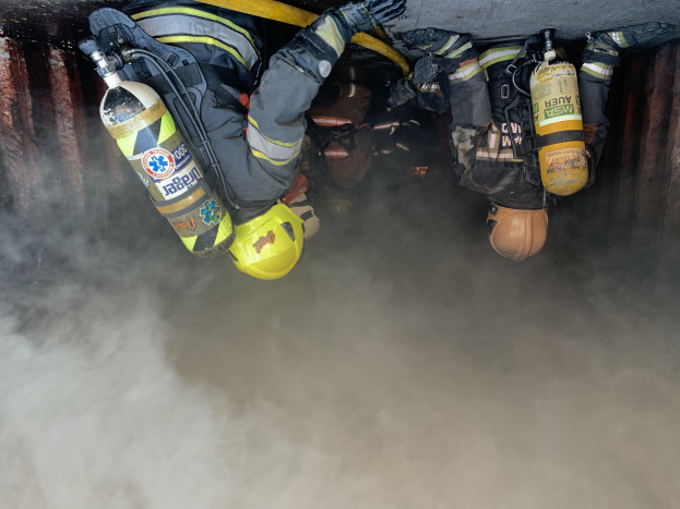 Feuerwehrleute in Schutzausrüstung arbeiten daran, ein Tunnelbrand zu löschen, bei dem Rauch aus der Tiefe aufsteigt.
