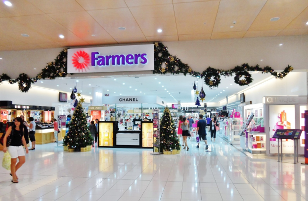 Menschen, die durch einen Weihnachtsdekorationen Einkaufszentrum mit beleuchteten Bäumen, Weihnachtsdekorationen und einer Deckenanzeigetafel gehen, einige mit Einkaufstaschen.