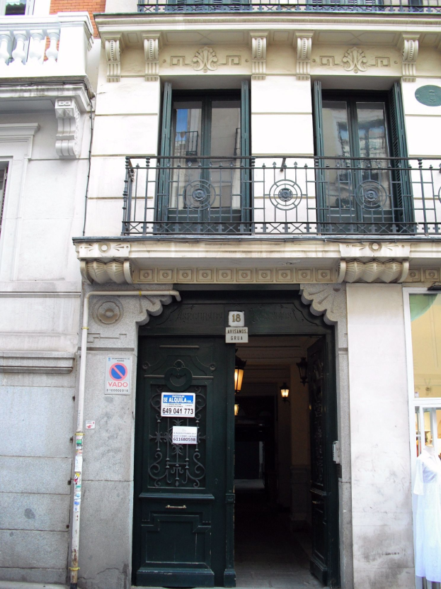 Ein Gebäude mit einer grünen Tür, Fenstern, Geländern, Lampen, Texttafeln, einem Rohr und anderen Objekten, mit einer Straße unten.