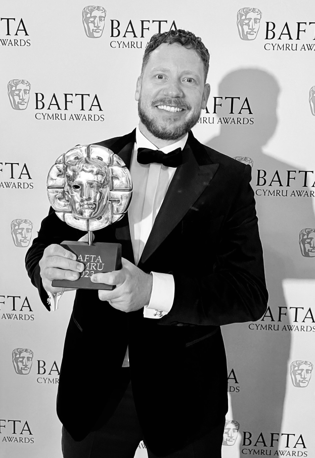 Ein Mann im Smoking, der eine BAFTA-Trophäe hält und vor einer Tafel mit der Aufschrift 'BAFTA Awards 2018' steht.