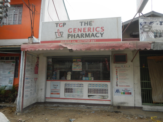 Außensicht der "Generics Apotheke" mit umgebenden stadtischen Elementen unter einem klaren blauen Himmel.