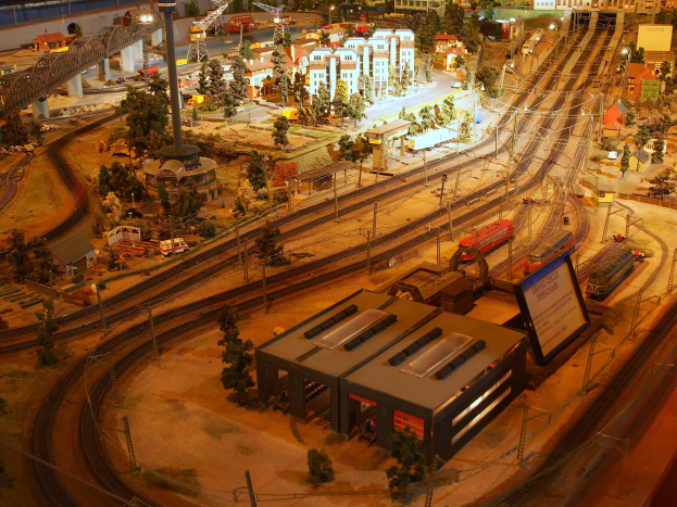 Eine detaillierte Modellbahnausstellung in einem Museum, mit Gebäuden, Bäumen, Schienen, Fahrzeugen, Pfählen, Lichtern und Platten, die eine belebte Stadtlandschaft nachahmen.