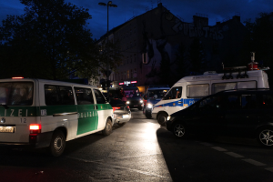 Eine Gruppe von Polizeiwagen, einschließlich eines Vans, Autos und Rades, die nachts auf der Seite einer Straße geparkt sind, mit Gebäuden, Bäumen, Laternenpfählen und einem sternenklaren Himmel im Hintergrund.