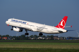 Turkish Airlines Airbus A330-300 startet von Frankfurt Airport mit Gras darunter, Gebäuden und Bäumen im Hintergrund, Windmühlen in der Ferne und einem klaren blauen Himmel.