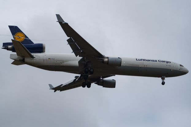 Ein Lufthansa Cargo Boeing 777-300ER im Flug, mit sichtbarem Text an der Seite und weißen Wolken am Himmel.