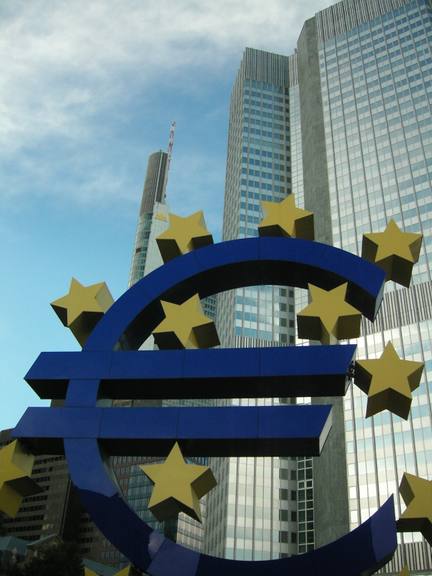 Das Euro-Zeichen vor dem Hauptquartier der Europäischen Zentralbank in Frankfurt, Deutschland, umgeben von Bäumen unter einem bewölkten Himmel.