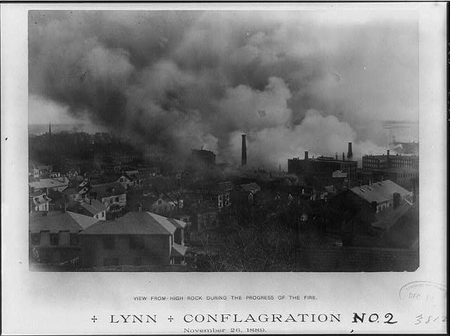 Schwarz-weißes Foto einer Stadt mit Rauch, der aus Gebäuden und Bäumen aufsteigt, mit der Beschriftung "Lynn und Conflagration No. 2" unten.