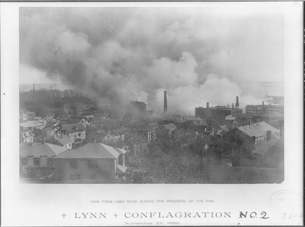 Schwarz-weißes Foto einer Stadt mit Rauch, der aus Gebäuden und Bäumen aufsteigt, mit der Beschriftung "Lynn und Conflagration No. 2" unten.