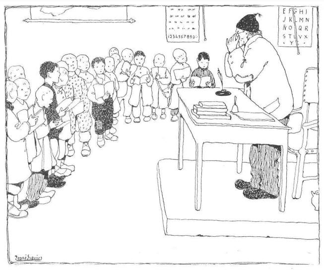 Ein Mann sitzt an einem Schreibtisch mit Büchern und Gegenständen vor einer Gruppe von Kindern, während Papiere mit Text an der Wand hinter ihm hängen.