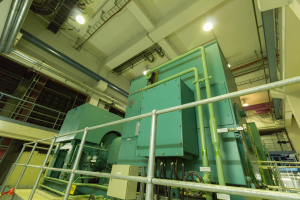 Eine große Wärmetauscher-Maschine in einem Gebäude, umgeben von Geländern, Rohren, Lampen und anderen Gegenständen, mit zahlreichen Rohren und Ventilen verbunden.