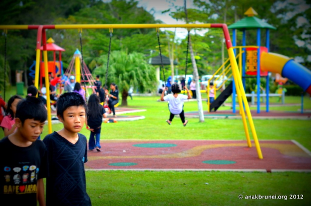 Kinder auf Spielplatzgeräten in einem Park mit Bäumen im Hintergrund