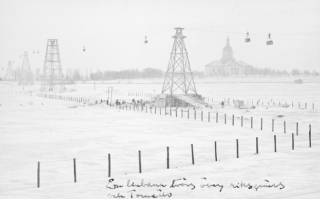Schwarze-Weiß-Foto eines Skilifts in einer verschneiten Wiese mit Stützpfählen und Drähten, umgeben von Bäumen und einem Gebäude im Hintergrund, mit Text am unteren Rand.