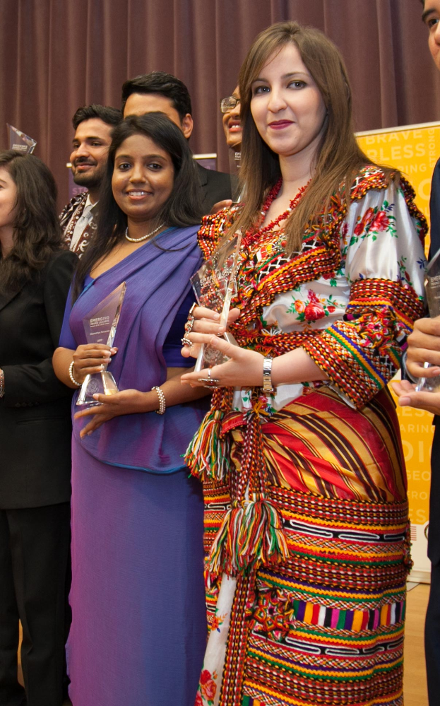 Eine Gruppe von Menschen auf einer Bühne mit einer Frau in der Mitte, die eine Trophäe hält, hinter einem Vorhang mit einer Tafel, auf der "Bravo Segen Award Gewinner" steht.