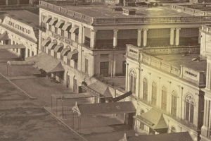 Schwarzes und wei├čes Foto einer Stra├če mit Geb├Ąuden, Fenstern, S├Ąulen, Namensschildern, Hütten und Masten.