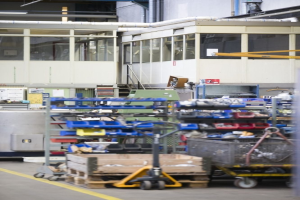 Lagerinneres mit verschiedenen Geräten einschließlich fahrbaren Wagen, Schränken und einer Box, mit einer Glasfensterwand und Rohren im Hintergrund.
