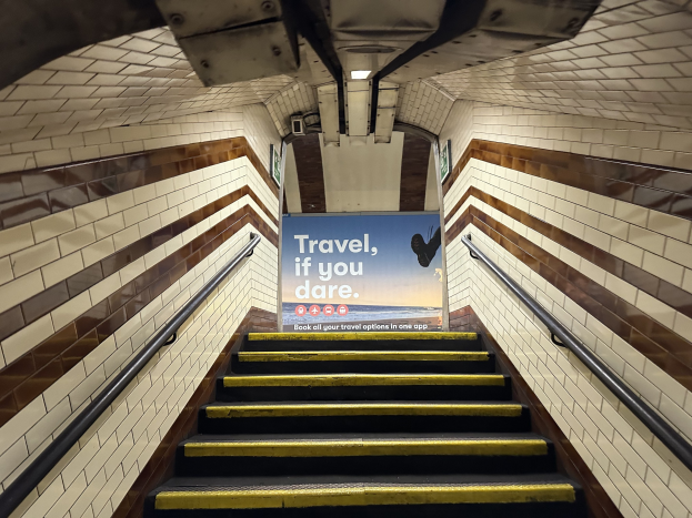 Eine Treppe in einer U-Bahn-Station mit einem Schild, das oben 'Reise, wenn du wagst' trägt, flankiert von Geländern und sichtbaren Stationwänden im Hintergrund.