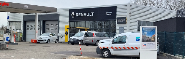 Ein Renault-Autohaus mit parkenden Autos davor, umgeben von einem Metallzaun, einem Schild, Pfählen, Bäumen und einem bewölkten Himmel.